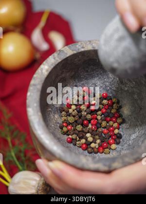 Hände Schleifen gemischter Pfefferkörner in Steinmörtel und Stößel, Lebensmittelzubereitung Stockfoto