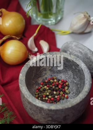 Nahaufnahme von Steinmörtel mit gemischten Pfefferhörnern und frischen Kochzutaten Stockfoto