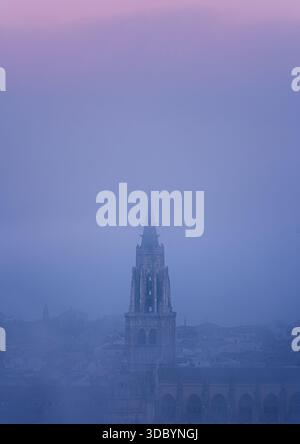 Vertikaler Blick auf den Turm der Kathedrale von Toledo, der aus dichtem Morgennebel auftaucht. Minimale Komposition und ruhige Pastelltöne. Stockfoto