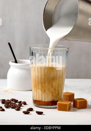 Großaufnahme von Karamell Latte Kaffeeglas auf weißem Tischhintergrund, Prozess der Herstellung von Frappe Stockfoto