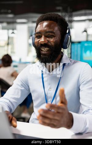 Fröhlicher Geschäftsmann, der bei Videokonferenzen mitarbeitet, Ideen austauscht und Projekte mit Kollegen aus der Ferne plant. Schwarzer männlicher Mitarbeiter, der virtuelles globales Webinar auf digitalen Geräten anhört. Stockfoto