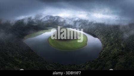 Ein ikonischer Blick aus der Vogelperspektive auf einen sich windenden Fluss, der teilweise von weichem Morgennebel bedeckt ist, der durch das Tal strömt. Die Kurven des Flusses zeichnen ag aus Stockfoto