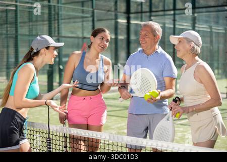 Ältere Männer und Frauen und ihre Töchter stehen und plaudern vor der Padel-Praxis Stockfoto
