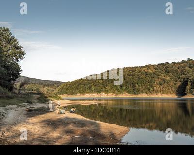 GARAS, SERBIEN - 23. AUGUST 2025: Angler fischen von einem Sandpunkt am Garasko Jezero, auch Gardasee genannt, im Westen Serbiens. Ruhiges Wasser und bewaldete h Stockfoto