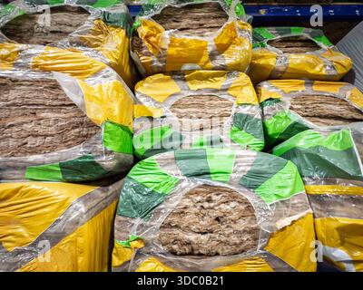 Stapel von Isolierschläuchen aus Mineralwolle, die in Kunststoffmarkenplatten auf den Regalen des Lagers gewickelt sind. Das Fasermaterial für thermische und akustische Leistung Stockfoto