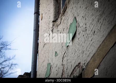Nahaufnahme von abblätterndem grünem Putz auf einer alten Wohnfassade, mit rissigem Stuck und verwitterter Wandstruktur durch ein Metallabflussrohr, das Negl veranschaulicht Stockfoto