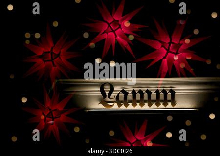 Adventsatmosphäre mit Girlandensternen, roten Lichtsternen, Abendstimmung in Rot und Gold, Lammbuchstaben in Goldbraun, Bokeh-Lichtkreisen, vor Christma Stockfoto