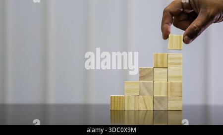 Holzblock von Hand auf Stufenpyramide platzieren, das Wachstumskonzept repräsentiert Stockfoto
