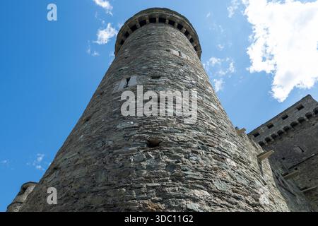 Flacher Blick auf den mittelalterlichen Steinturm der Burg Fenis im Aostatal mit Zinnen und Pfeilschlitzen gegen den Sommerhimmel. Stockfoto