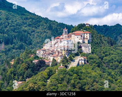 Blick aus der Vogelperspektive auf ein Dorf auf einem Hügel in der Nähe von Varese, Italien, umgeben von einem Kirchturm und Steinhäusern über dichten Wäldern. Stockfoto