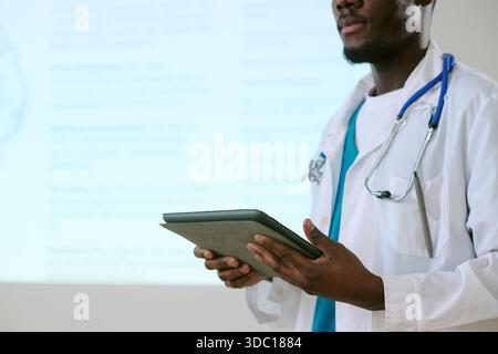 Junger Erwachsener Schwarzer Mann Doktor hält Digital Tablet während der medizinischen Präsentation Stockfoto