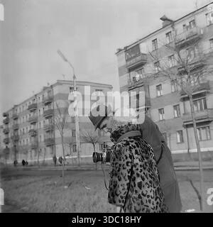 Sloviansk, Ukrainische SSR, UdSSR, 1960er Jahre Ein Archivfoto, das einen berührenden Familienmoment festhält: Der Fotograf Michail Iljitsch Kravelis bringt seiner Tochter Inna Mikhailovna die Verwendung einer professionellen Mittelformatkamera bei. Der Vater beugt sich nach unten und zeigt dem Kind den Sucher. Das Mädchen trägt einen modischen Mantel mit Leopardenmuster und einen warmen Hut. Der Hintergrund zeigt typische sowjetische Wohnarchitektur. Eine herzerwärmende Szene der Eltern und des Hobbys im friedlichen Donbass Stockfoto