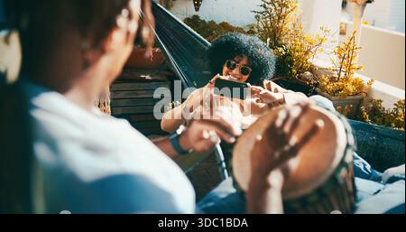 Draußen, Trommeln oder glückliches Paar mit Telefon in der Hängematte, Musikinstrument spielen oder Video auf dem Balkon aufnehmen. Mobile App, Live-Stream oder Menschen Stockfoto