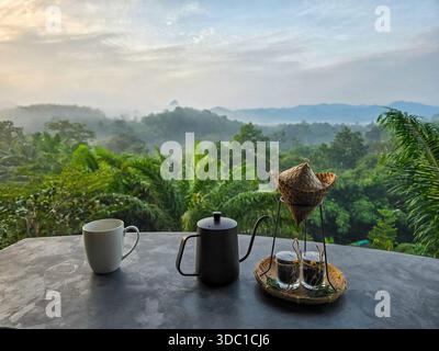 Genießen Sie einen friedlichen Morgen in Khao Sok, Thailand, während die Sonne über dem dichten Regenwald aufgeht. Auf einem Tisch erwartet Sie ein traditionelles Teeset mit Blick auf den Lus Stockfoto