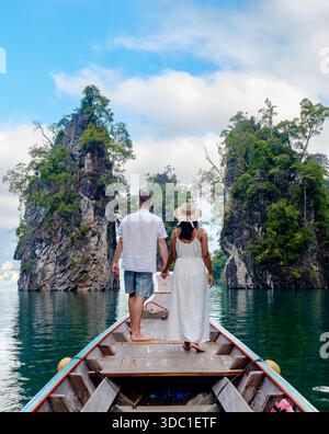 Paare stehen Hand in Hand auf einem Boot, umgeben von üppigen grünen Klippen und ruhigen Gewässern des Cheow Lan Lake. Dieser malerische Ort in Khao Sok, Thai Stockfoto