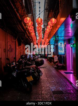 Bangkok, Thailand, 19. November 2025, von oben hängen leuchtende rote Laternen, die ein warmes Leuchten auf einer engen Gasse in Chinatown ausstrahlen. Neonschilder und geparkte Roller tragen zur lebhaften Atmosphäre bei. Stockfoto