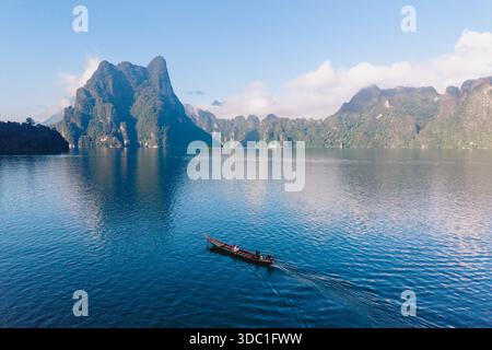 Eine ruhige Szene am Cheow Lan Lake bietet ein traditionelles Holzboot, das über das kristallklare Wasser gleitet. Khao Sok Thailand Stockfoto
