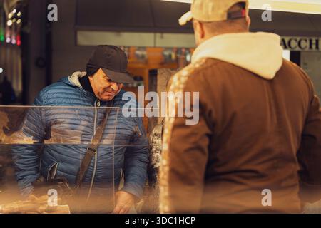 Rovigo, italien 18. dezember 2025: Kunde prüft Produkte und chats mit dem Anbieter an einem Straßenmarkt in der Stadt, schnörkellose Einkaufsmöglichkeiten im Alltag und kleine Unternehmen Stockfoto