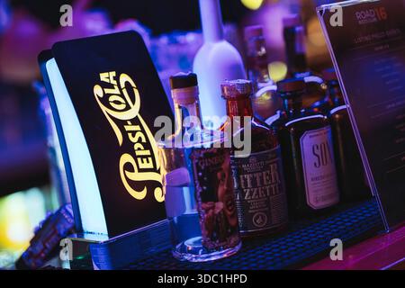 Rovigo, italien 18. dezember 2025: Das beleuchtete pepsi-Cola-Schild leuchtet über Spirituosenflaschen auf einer Bar, während warme Neonreflexe ein lebendiges Nachtli erzeugen Stockfoto