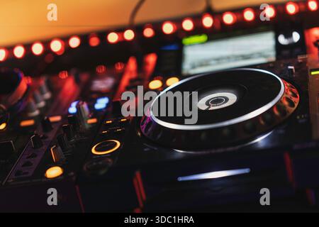Rovigo, italien 18. dezember 2025: dj-Mischpult mit Plattenspieler, beleuchtet von roten und orangen Lichtern in einem Nachtclub, schafft Party- und Musikatmosphäre Stockfoto