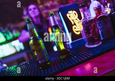 Rovigo, italien 18. dezember 2025: Bar mit erfrischenden Bierflaschen und Spirituosen unter leuchtenden Neonlichtern, bereit für Nachtleben und Unterhaltung Stockfoto