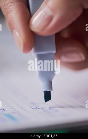 Weibliche Hand, die Markierer auf Papier hält, Nahaufnahme mit Fingernägeln und Stiftspitze, Frau, die Handschreibaufgaben auf dem Raster-Notizbuch ausführt, Fokus auf Finger und Stift Stockfoto