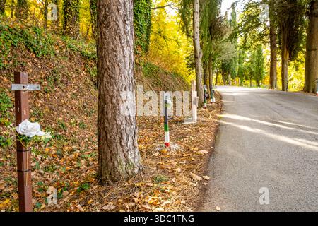 Gedenkstätten am Straßenrand markieren einen düsteren Abschnitt der Straße durch einen Herbstwald und bieten eine stille Hommage an die durch Unfälle verlorenen Leben Stockfoto