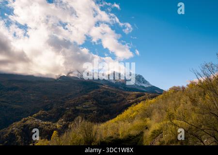 Jahreszeiten wechseln mit einer herbstlichen Landschaft mit schneebedeckten Bergketten, großem blauen Himmel und weißen Wolken über grün-gelben Hügeln Stockfoto