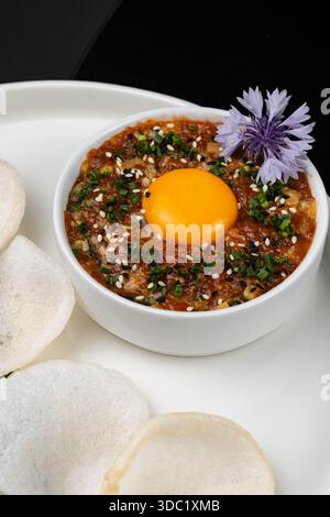 Tatar mit Eigelb und Reischips auf einer weißen Platte isoliert Stockfoto