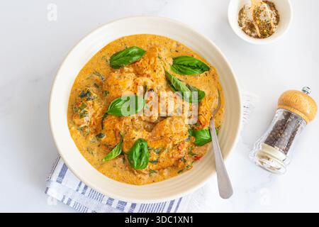 Italienisches cremiges toskanisches Huhn mit Spinat und sonnengetrockneten Tomaten garniert mit frischem Basilikum Stockfoto