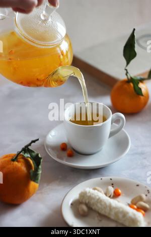 Sanddorntee wird aus einer transparenten Teekanne in eine Tasse gegossen Stockfoto