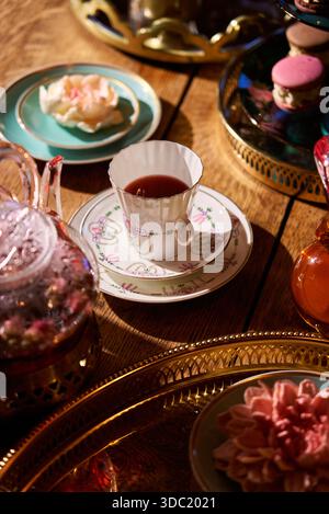 Teetasse und Topf auf Holztisch mit farbenfrohen Gebäckstücken und Blumen Stockfoto