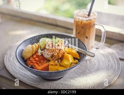 Schüssel mit Mango, Papaya, Banane, Limette und Müsli mit Eis-Cappuccino Stockfoto