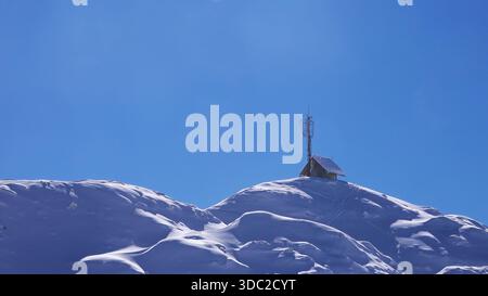 Kleine Kabine mit Antenne auf verschneiten Berggipfeln unter klarem blauem Himmel, selektiver Fokus Stockfoto