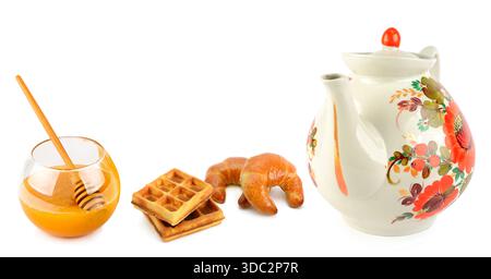 Eine charmante Anordnung aus einer Teekanne mit Blumenmuster, frischen Waffeln und flüssigem Honig auf einem sauberen weißen Hintergrund. Stockfoto