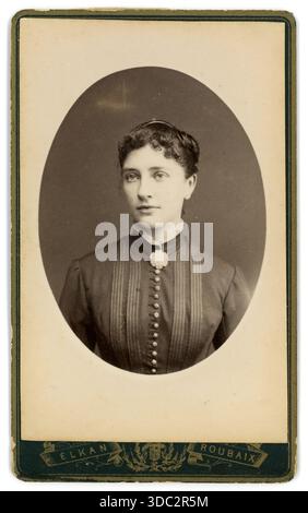 Originales viktorianisches Carte de Visite (Visitenkarte oder CDV) ovales Porträt einer schönen französischen Frau mit Blumenbrosche, Knöpfen ihrer Bluse oder ihres Kleides, gekräuselten oder gewellten Fransen. Foto des niederländischen Fotografen Elkan (Jacob Huisman) 74, Rue Pellart, 59100 Roubaix, Frankreich, um 1880 Stockfoto