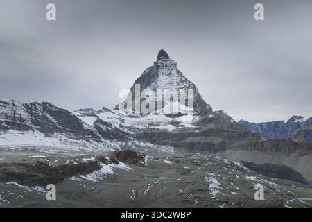 Aus der Vogelperspektive auf den majestätischen Gipfel des Matterhorns, der durch die Wolken durchsticht, seine schneebedeckten Hänge im Kontrast zum rauen Gelände darunter, Zermatt, Va Stockfoto