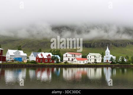Farbenfrohe Häuser und blaue Kirche spiegeln sich im Wasser in Seydisfjordur, Ost-Island. Stockfoto