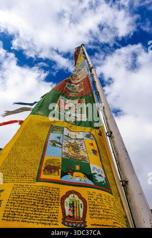 Bunte buddhistische Gebetsfahnen ragen auf einem hohen Fahnenmast in den Himmel und flattern in der Brise mit Blick auf den hellen, bewölkten Himmel Stockfoto