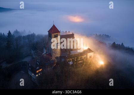 Aus der ätherischen Nebelumarmung erhebt sich ein Blick auf die mittelalterliche Wachenburg, deren alte Steine von warmem Licht gegen die Schwächung beleuchtet werden Stockfoto