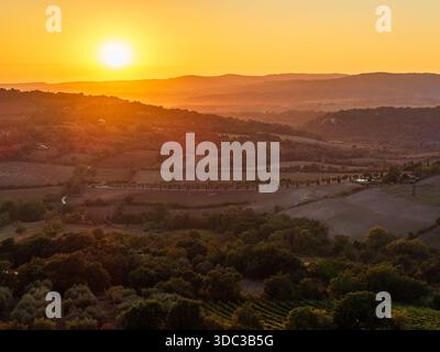 Aus der Vogelperspektive auf den Sonnenaufgang über den sanften Hügeln und üppigem Grün, die Landschaft in warmen Gold- und Bernsteintönen, Saturnia, Toskana, Ital Stockfoto
