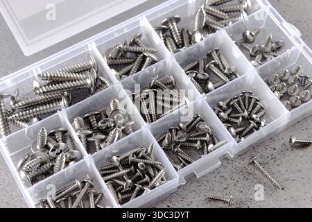 Satz mit verschiedenen Schrauben, die in einer Kunststoffbox auf grauem Hintergrund angeordnet sind. Hardwaretools-Konzept. Stockfoto