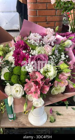 Lebhaftes Bouquet mit Rosen, Chrysanthemen, Alstroemeria und Lisianthus in Rosa-, Violett- und Weißtönen, in weichen Pastellhüllen. Stockfoto