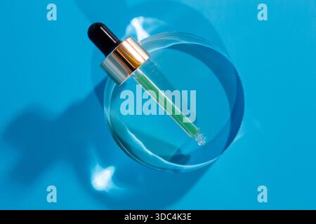 Glaspipette mit Hyaluronsäure auf Glaskreisträger, blauer Hintergrund. Kosmetikkonzept Stockfoto