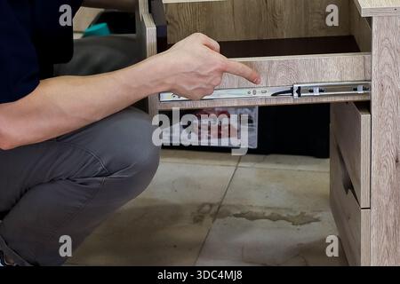 Nahaufnahme der Hand, die auf den Schiebemechanismus der installierten Schublade zeigt. Nahaufnahme der Hand einer Person, die auf die Schiene der kugelgelagerten Schublade aus Metall zeigt, die auf W montiert ist Stockfoto