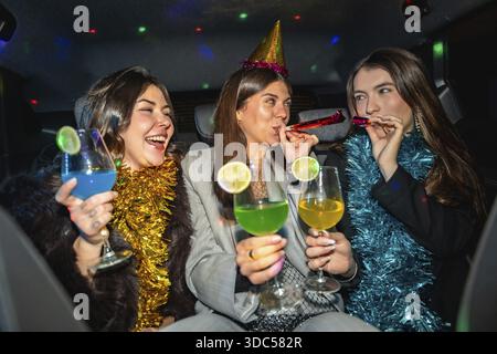 Junge Freundinnen feiern Silvesterabend oder besondere Anlässe, Spaß im Auto haben, bunte Cocktails und Partygebläse genießen und festlich feiern Stockfoto