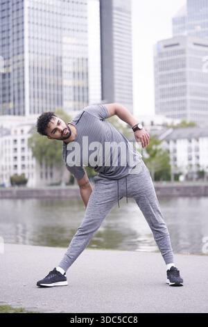Mann, der Stretching-Übungen in Sportbekleidung am Main in der Großstadt Frankfurt am Main macht, Routinegewohnheiten für Outdoor-Workouts, marokkanisch e Stockfoto