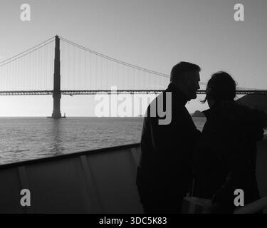 Silhouettenpaare stehen an Bord einer Fähre mit der Golden Gate Bridge, die sich über den Hintergrund über der San Francisco Bay erstreckt. Stockfoto
