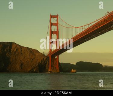 Die Golden Gate Bridge überspannt die Bucht von San Francisco bei Sonnenuntergang, vom Wasser aus mit warmem Licht auf der berühmten roten Hängebrücke. Stockfoto