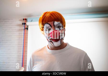 Lächelnder Mann mit Clown-Make-up, roter Nase und oranger Perücke Stockfoto